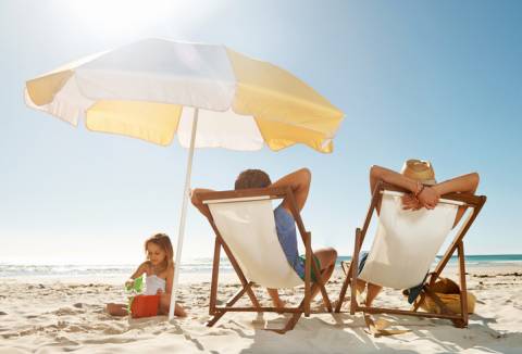 two adults lounging in yellow stripped beach chairs with matching umbrella and young daughter playing in sand two adults lounging in yellow stripped beach chairs with matching umbrella and young daughter playing in sand